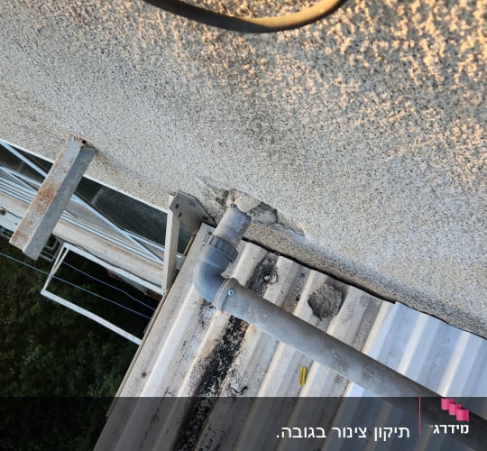 צינור פלסטיק אפור מחובר לקיר מעל גג מתכת גלי